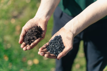 Two hands holding biochar is a grassy field