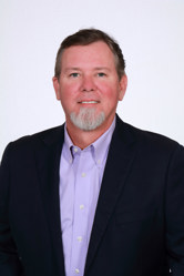 A portrait of a man in a purple dress shirt and a suit jacket.